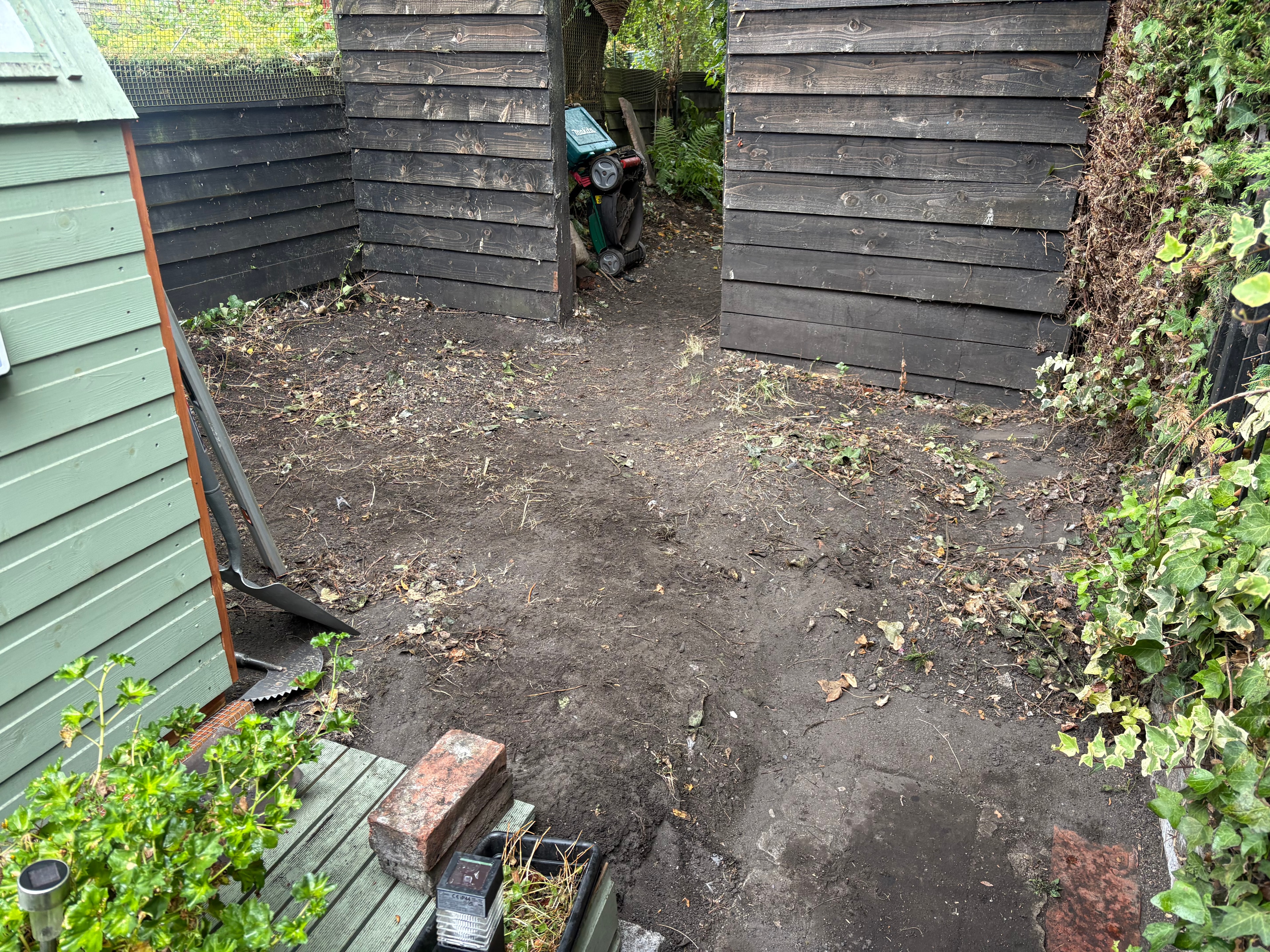 Neglected outdoor area with bare soil and dark timber fencing before patio installation